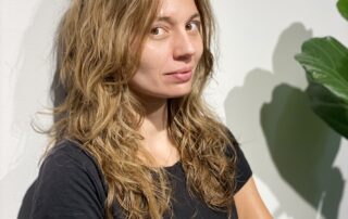 Középhosszú, világosbarna göndör haj lágy átmenetes vágással és hullámzó tincsekkel
